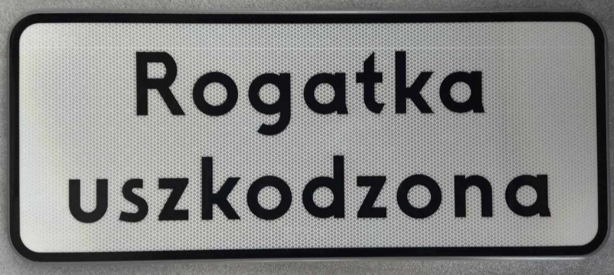 Tabliczka pod znak drogowy T z treścią "Rogatka uszkodzona".